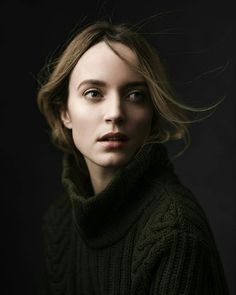 a woman in a green sweater with her hair blowing in the wind, looking directly into the camera