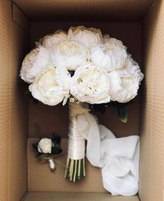 a bouquet of white peonies in a cardboard box with the bride's dress