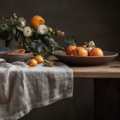 two bowls filled with oranges on top of a wooden table next to a white cloth