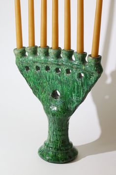 a green ceramic menorah with candles sticking out of it's sides, on a white background