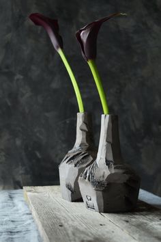 two vases with flowers in them sitting on a wooden table next to a wall