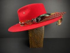 The Memphis Fedora This stunning red fedora is inspired by the sounds and sights of memphis. Featuring a gorgeous paisley silk fabric hat band, topped with our faux suede band with red coral details. Featuring our distinctive handstitched star. Feathers include a combination of both rooster asnd pheasant. Available in Large 59cm only. *Please note that this is a 'stiff' style hat* Bohemian Red Fedora With Flat Brim, Red Fitted Hat For Festival, Western Style Red Fedora With Short Brim, Red Bohemian Fedora With Flat Brim, Red Fedora With Curved Brim For Rodeo, Red Western Fedora With Short Brim, Adjustable Red Fedora Hat Band, Red Curved Brim Fedora For Rodeo, Red Fedora Hat For Festivals