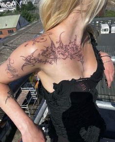 a woman with tattoos on her back standing next to a train track and looking off into the distance