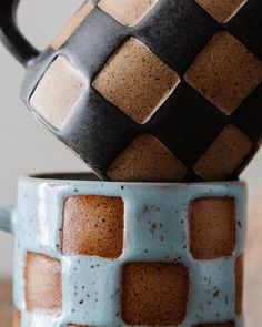 two coffee mugs stacked on top of each other, one has a black and white checkerboard design