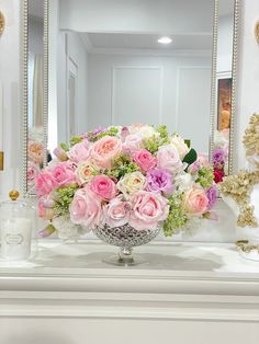 a vase filled with pink and white flowers sitting on top of a dresser next to a mirror