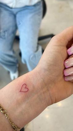 a woman's arm with a small heart tattoo on her left wrist and pink nail polish