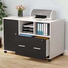 an office desk with two drawers and a printer on it's side, next to a potted plant