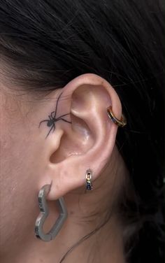 a woman with a spider tattoo on her ear and behind the ear is a pair of hoop earrings