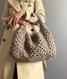 a woman wearing a trench coat holding a crocheted purse