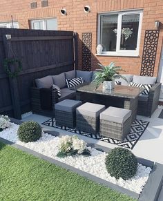 an outdoor living area with couches, tables and plants on the grass in front of a brick building