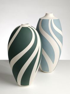 two green and white vases sitting side by side on a counter top, one with wavy lines painted on it