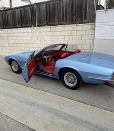 a blue car parked in front of a building with its doors open and the door opened