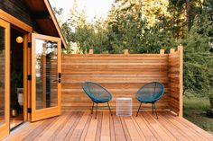 two blue chairs sitting on top of a wooden deck next to a wall with wood slats