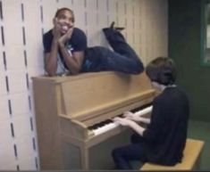 two young men sitting at a piano in a room with white tiles on the walls