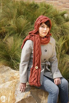 a woman sitting on top of a rock wearing a scarf