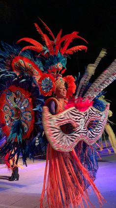 a woman in colorful costume with feathers on her head and zebra print mask, walking down the street at night