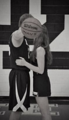 two girls in black and white basketball uniforms holding a ball with the word wilson on it