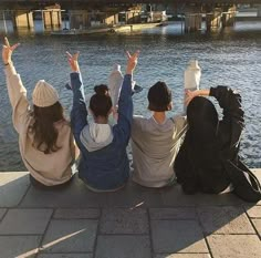 three women sitting on the ground with their arms in the air while looking at water