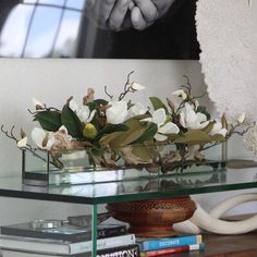 a glass shelf with flowers and books on it in front of a large framed photo