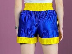 a woman in blue and yellow shorts with her back turned to the camera, standing against a purple background