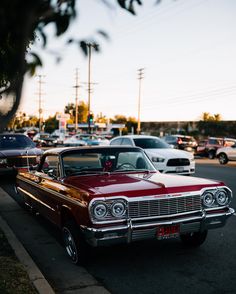 an old red car is parked on the side of the road in front of other cars