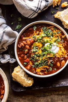 a bowl of chili with sour cream on top and cornbreads next to it