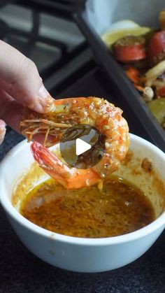 a person dipping some food into a bowl with shrimp in it and another dish on the side