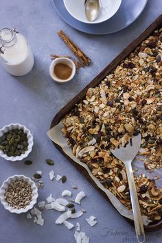 a baking pan filled with granola next to bowls of nuts and other food items