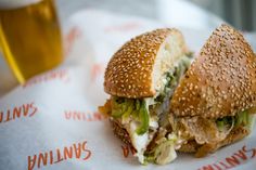 a sandwich cut in half sitting on top of a paper wrapper next to a glass of beer