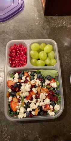 a plastic container filled with fruit and cheese on top of a table next to a bowl of grapes