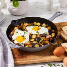 two fried eggs are in a skillet on a cutting board next to bread and vegetables