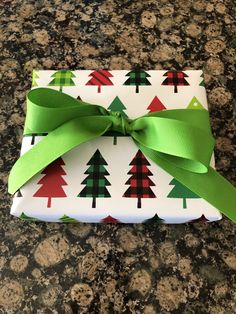 a present wrapped in white paper with green ribbon and trees on the wrapping paper is sitting on a granite countertop