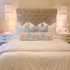 a white bed with two pillows on top of it and some pictures above the headboard