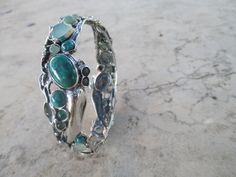 From Porans collection: Sterling Silver Bracelet with 28 stones inlaid. Turquoise, Labradorite, Green quartz, opalite & Aventurine. The bracelet can be ordered with a combination of stones. Please check with me what options are available Dimensions: Max Width: 20 mm bangle size- 63 mm Please let me know if you have any questions. our jewelry shop on Etsy: http://www.etsy.com/shop/Porans Thank you for visiting our shop. Please visit my shop policies for additional information Unique Chrysocolla Bracelets As Gifts, Unique Green Gemstone Bracelets, Unique Cabochon Bangle Bracelets, Spiritual Green Bangle Cuff Bracelet, Handmade Green Sterling Silver Bangle, Green Bracelet With Stone Setting As Gift, Green Bangle With Natural Stones For Gift, Green Bangle Bracelets In Fusion Style, Green Gemstone Bangle Cuff Bracelet