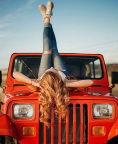 a woman laying on the hood of a red jeep with her legs up in the air