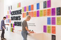 two people are standing in front of a wall with colorful notes on it that say change starts here