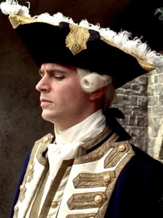 a man wearing a black and white hat with feathers on it's head is standing in front of a brick wall