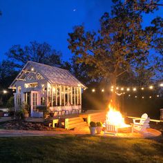 a lit up fire pit in front of a white house with lights strung around it