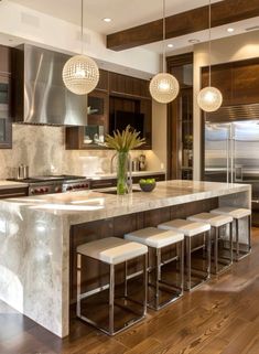 a large kitchen with marble counter tops and wooden flooring that has pendant lights hanging from the ceiling