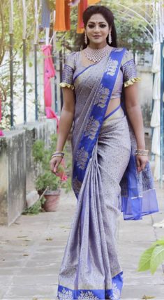 a woman in a blue and silver sari walking down the street with her hand on her hip