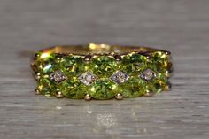 The Clayton: Stackable Peridot and Diamond Band in Yellow Gold. The ring features two rows of oval brilliant cut natural peridot set east to west across the center with four diamond-shaped sections set with natural round diamonds. Low set and well made,the ring is very comfortable to wear and the peridot are outstandingly matched to perfection. The ring is crafted in 14 karat yellow gold and is currently a finger size 7 3/4 yet can be adjusted to any finger size for an additional charge on reque Green Multi-stone Oval Diamond Ring, Green Oval Multi-stone Diamond Ring, Oval Green Multi-stone Diamond Ring, Oval Multi-stone Peridot Gemstones, Oval Peridot Multi-stone Jewelry, Oval Peridot Gemstones For Anniversary, Oval Green Diamond Ring With Gemstone Accents, Knot Ring, Diamond Shaped