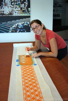 a woman is painting an orange and white table runner