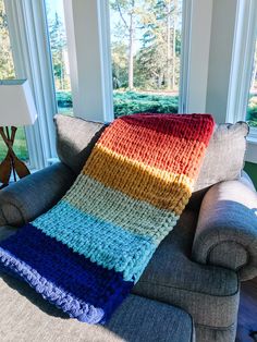 a multicolored crocheted blanket sitting on top of a couch next to a window