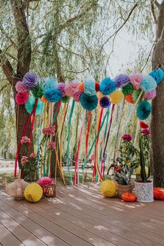 an outdoor party with colorful paper flowers and streamers on the tree trunk, in front of a wooden deck