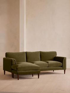 a green couch sitting on top of a hard wood floor next to a white wall