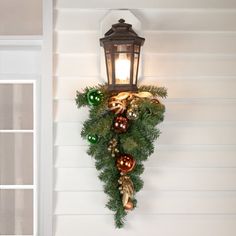 a lantern hanging from the side of a wall decorated with christmas ornaments and greenery