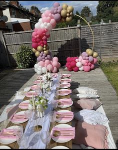 the table is set up with pink and gold plates, napkins, and balloons