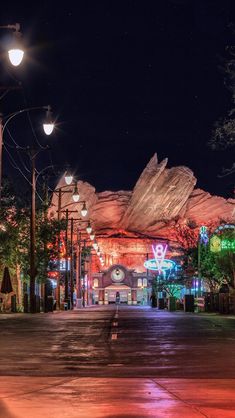 an empty city street at night with lights on the buildings and mountains in the background