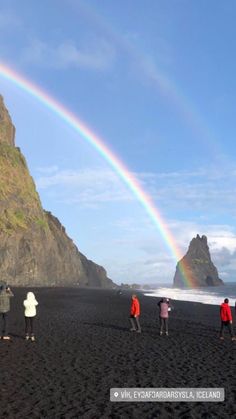 people are standing on the beach with a rainbow in the sky