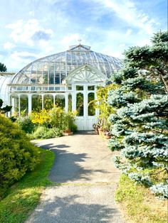 a walkway leading to a glass house with lots of plants and trees in the foreground